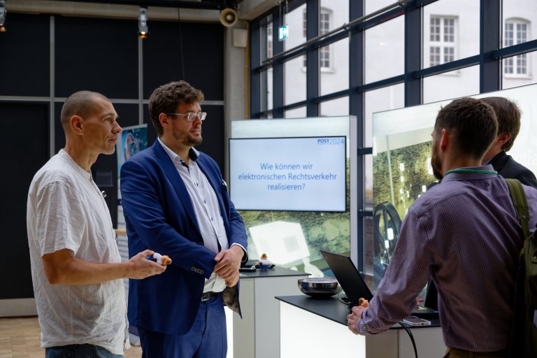Drei Personen stehen in einem modernen Raum und diskutieren über elektronischen Rechtsverkehr.