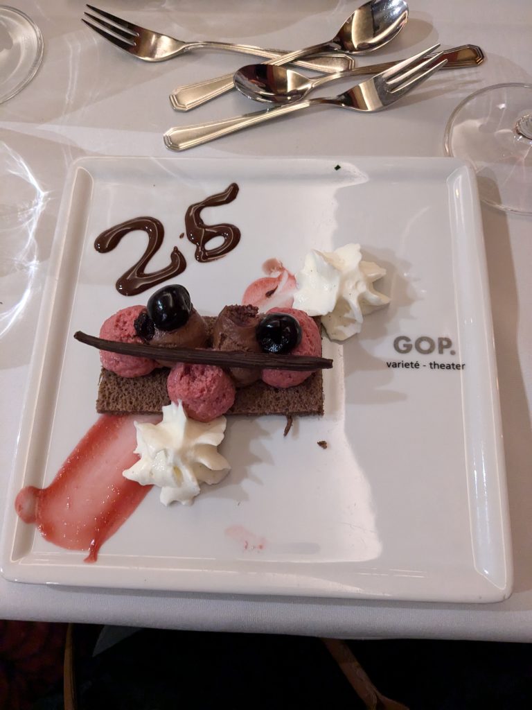 Ein Dessert auf einem weißen Teller mit Schokoladendekor, Sahne und einer Zahl 25.